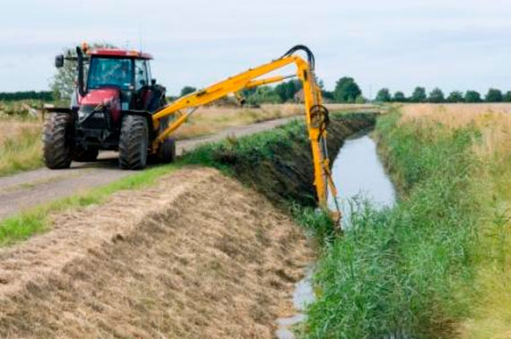 A tractor travels along a drainside road using its outreached hydraulic arm to carry out routine weed cutting and flailing of the drain’s bank sides