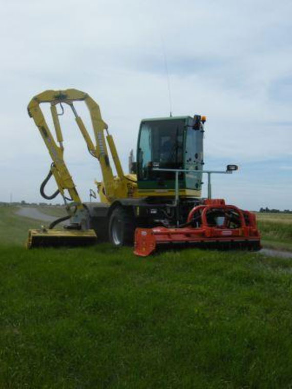 Cutting the grass verges on either side of a public highway, which travels along the top of a bank running between two drains