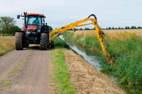 A tractor travels along a drainside road using its outreached hydraulic arm to carry out routine weed cutting and flailing of the drain’s bank sides