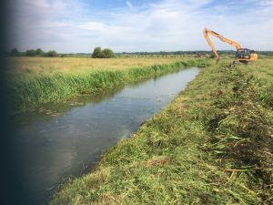 A tracked excavator uses its long-reach hydraulic arm to carry out routine weed cutting and flailing of the drain’s bank sides