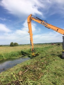 A tracked excavator uses its long-reach hydraulic arm to carry out routine weed cutting and flailing of the drain’s bank sides